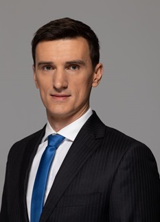 Mężczyzna w ciemnym garniturze, białej koszuli i niebieskim krawacie. Ma ciemne włosy. Jest to członek Zarządu do spraw Zarządzania Ryzykiem Adrian Kaim